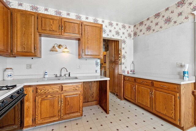 kitchen with a sink, light floors, brown cabinetry, range with gas cooktop, and wallpapered walls