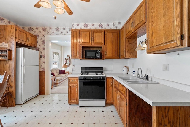 kitchen with wallpapered walls, gas range, freestanding refrigerator, black microwave, and a sink