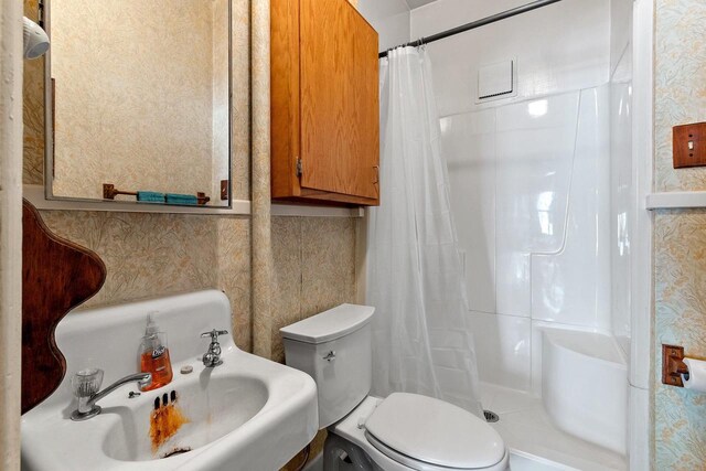 bathroom featuring curtained shower, a sink, toilet, and wallpapered walls