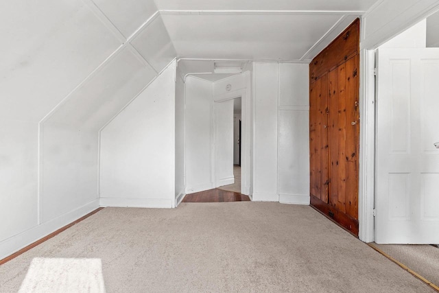 additional living space with carpet floors, a decorative wall, and lofted ceiling