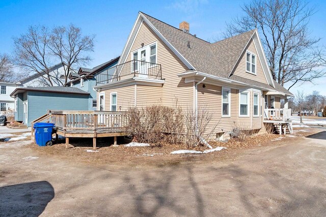 view of side of property featuring a chimney, roof with shingles, and a balcony