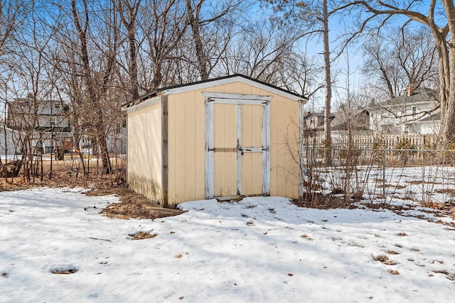 snow covered structure with an outdoor structure, a storage shed, and fence