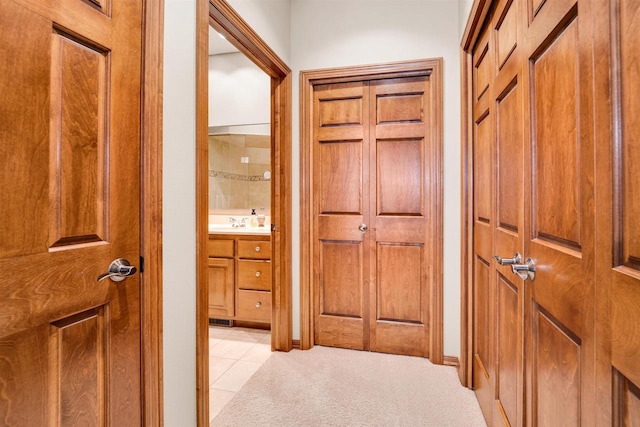 hallway with light carpet, light tile patterned floors, and a sink