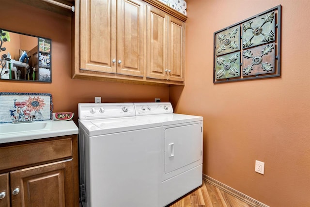 washroom featuring cabinet space, light wood-style flooring, washing machine and dryer, a sink, and baseboards