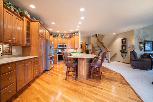 kitchen featuring a kitchen bar, appliances with stainless steel finishes, brown cabinetry, and open floor plan