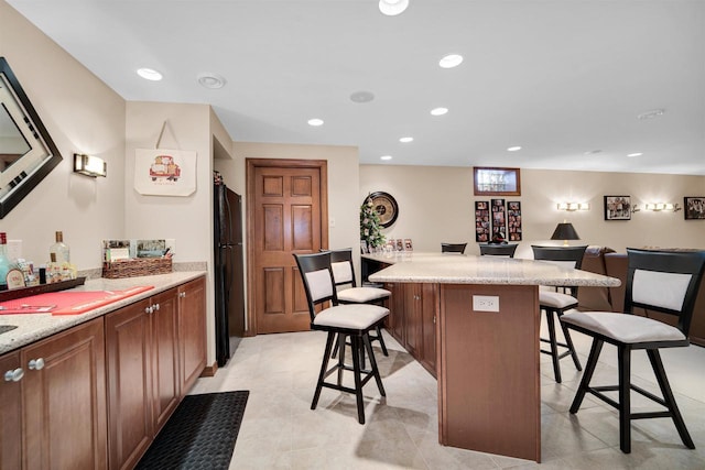 kitchen with recessed lighting, a breakfast bar, open floor plan, freestanding refrigerator, and a center island