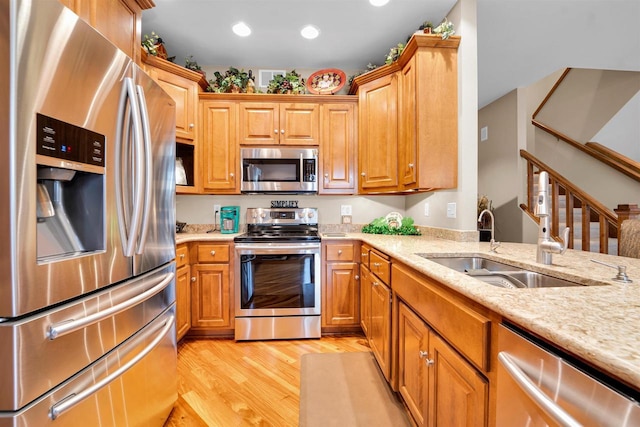 kitchen featuring stainless steel appliances, recessed lighting, a sink, light stone countertops, and light wood-type flooring