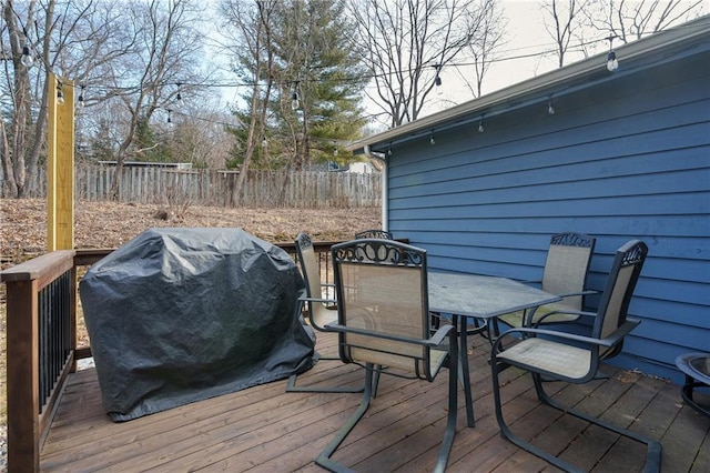 wooden terrace with outdoor dining space, a grill, and fence