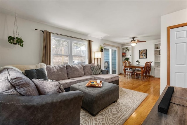 living area featuring built in features, a ceiling fan, and light wood-style floors