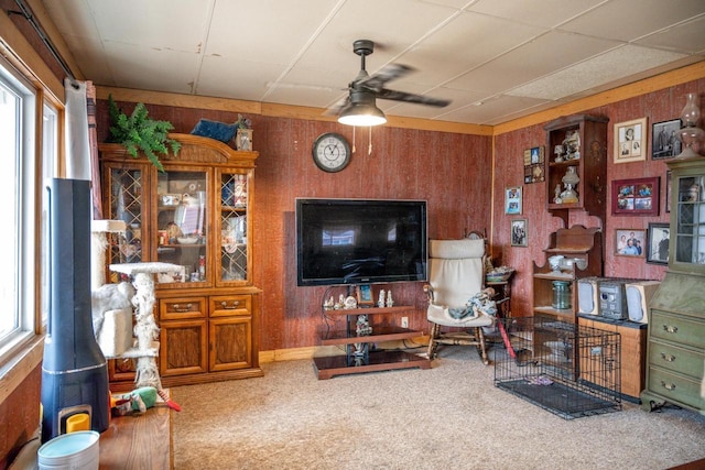 carpeted living room with ceiling fan, wood walls, and plenty of natural light