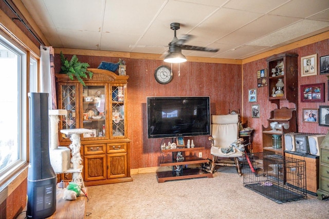 carpeted living room featuring ceiling fan, wooden walls, and a wealth of natural light