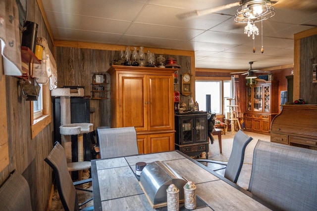 carpeted dining area with a drop ceiling, wood walls, and ceiling fan