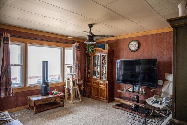 living room featuring carpet floors, ceiling fan, wooden walls, and a paneled ceiling