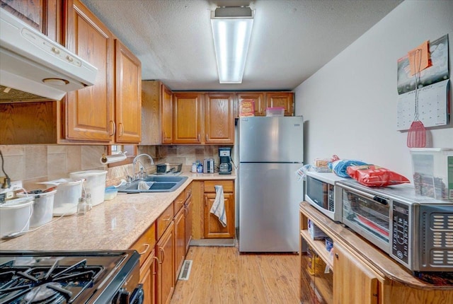 kitchen featuring visible vents, light wood-style flooring, stainless steel appliances, under cabinet range hood, and a sink