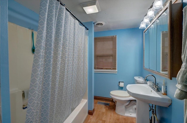 bathroom featuring baseboards, visible vents, toilet, wood finished floors, and shower / tub combo with curtain