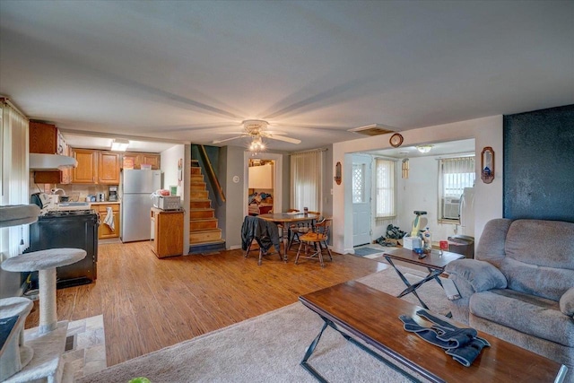 living room with light wood-type flooring, visible vents, stairway, and a ceiling fan