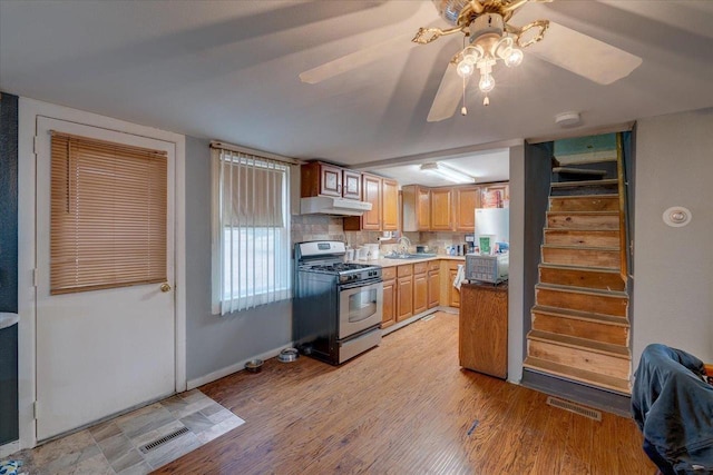 kitchen with stainless steel gas range oven, visible vents, light wood-style floors, under cabinet range hood, and a sink