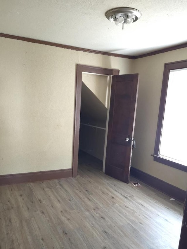 empty room featuring crown molding, a textured ceiling, baseboards, and wood finished floors