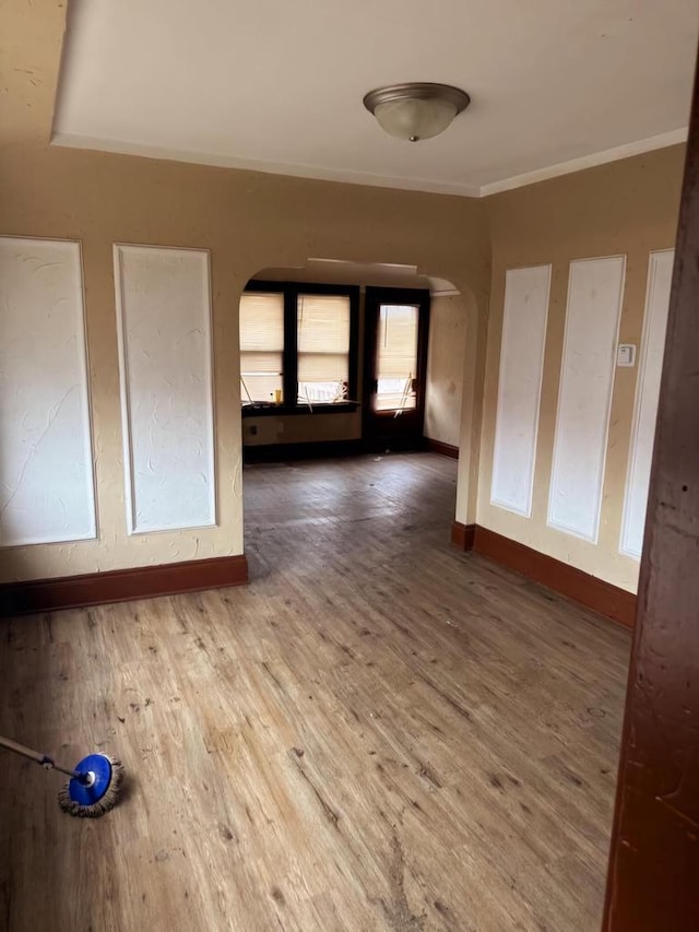 empty room featuring arched walkways, crown molding, baseboards, and wood finished floors