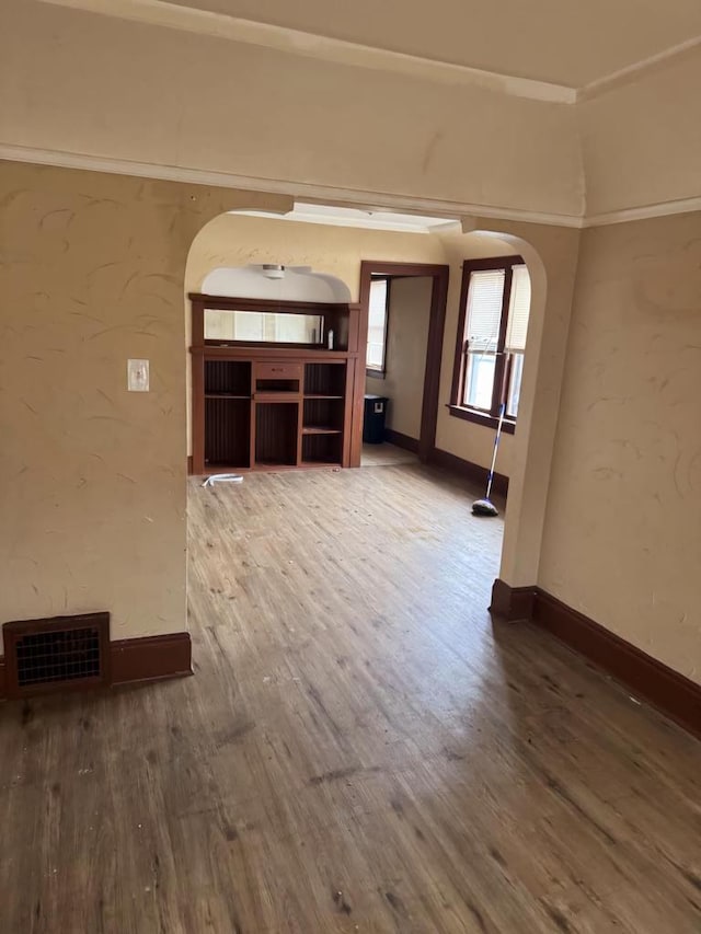 unfurnished living room with arched walkways, wood finished floors, visible vents, and baseboards