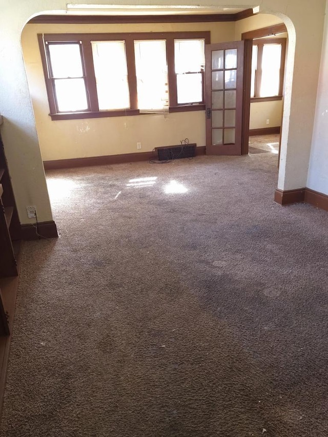 carpeted spare room with arched walkways, radiator heating unit, plenty of natural light, and baseboards