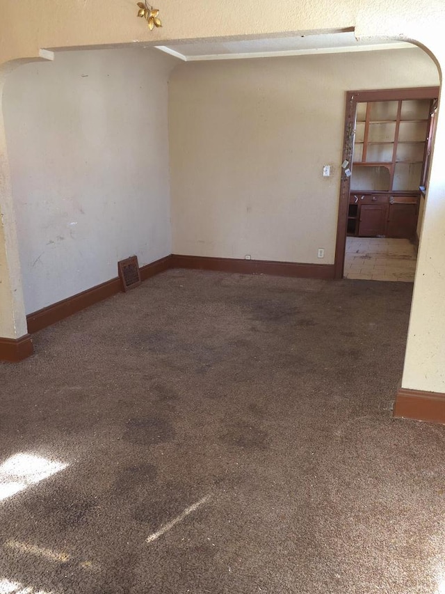 unfurnished room featuring carpet floors, arched walkways, and baseboards