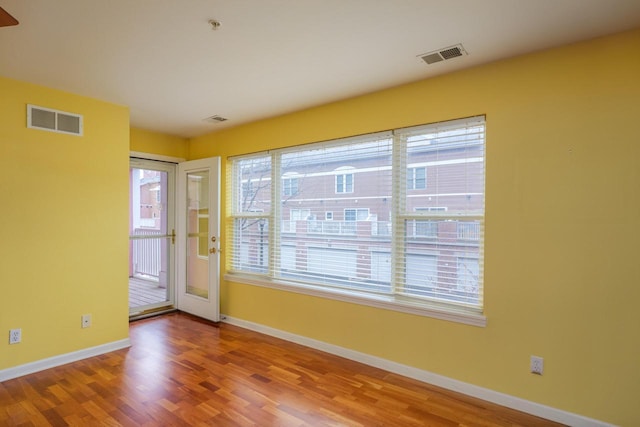 unfurnished room with wood finished floors, visible vents, and baseboards