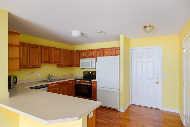 kitchen with appliances with stainless steel finishes, a peninsula, light countertops, open shelves, and a sink