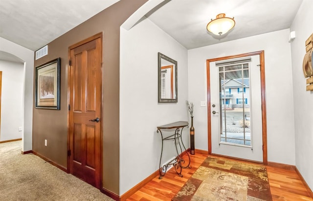 entryway with arched walkways, wood finished floors, visible vents, and baseboards