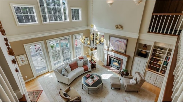 living area featuring a notable chandelier, a glass covered fireplace, a high ceiling, and wood finished floors