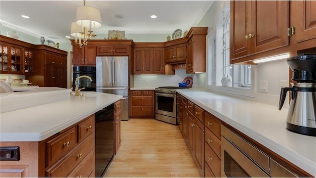 kitchen featuring light wood-type flooring, black appliances, ornamental molding, light countertops, and hanging light fixtures