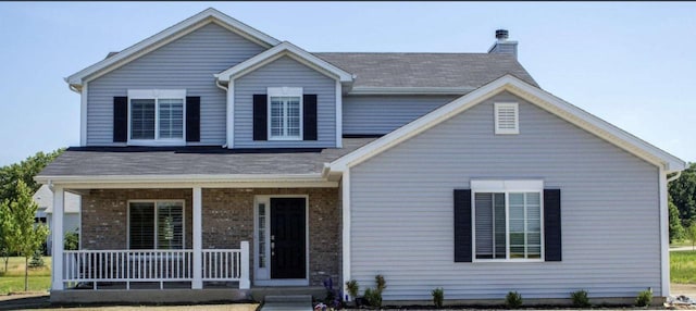 view of front of home featuring a chimney, a porch, and brick siding