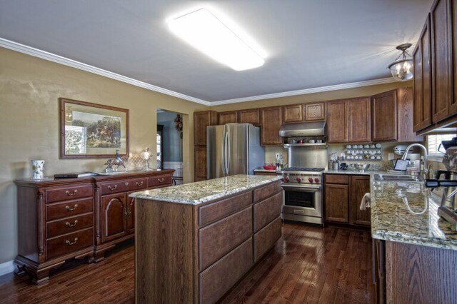 kitchen with light stone counters, dark wood-style flooring, stainless steel appliances, crown molding, and under cabinet range hood