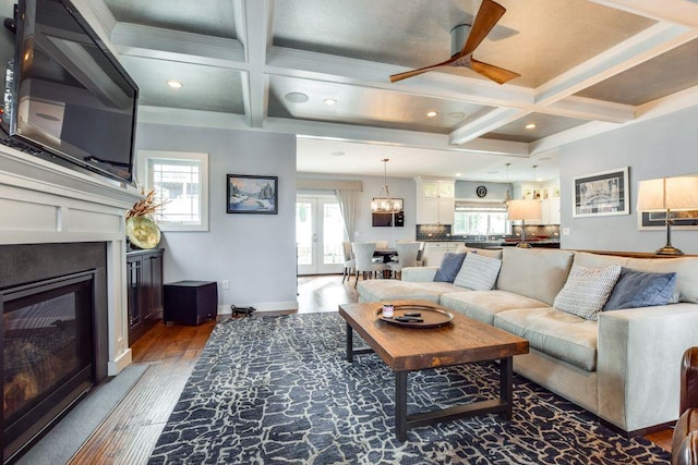 living area featuring coffered ceiling, wood finished floors, baseboards, french doors, and a glass covered fireplace