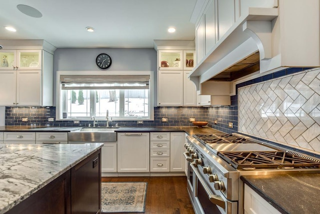 kitchen with white cabinets, range with two ovens, dark wood-style floors, dark stone countertops, and range hood