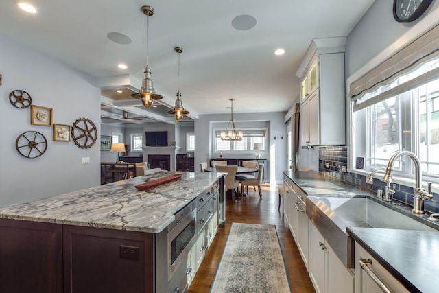 kitchen with a fireplace, a sink, tasteful backsplash, stainless steel microwave, and dark wood finished floors