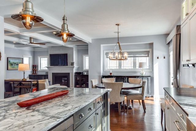 kitchen with light stone counters, dark wood-type flooring, beamed ceiling, a glass covered fireplace, and decorative light fixtures