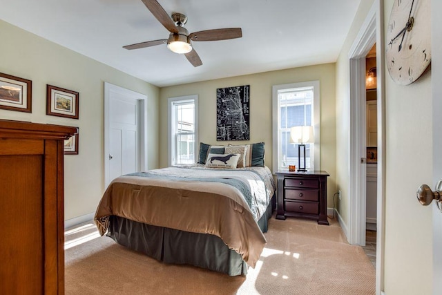 bedroom with light carpet, ceiling fan, baseboards, and ensuite bathroom