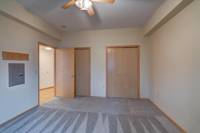 unfurnished bedroom with carpet flooring, a ceiling fan, baseboards, electric panel, and two closets