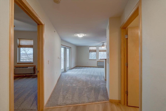 hall featuring a wall mounted air conditioner, carpet flooring, baseboards, and wood finished floors