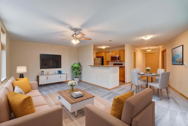 living area with light wood finished floors, a ceiling fan, and baseboards