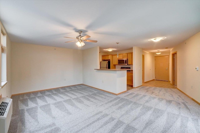 kitchen featuring light colored carpet, a peninsula, baseboards, fridge, and stainless steel microwave