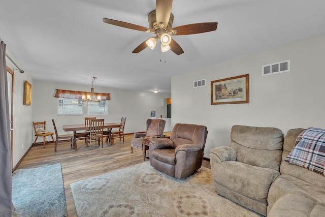 living room featuring visible vents, light wood-style flooring, baseboards, and ceiling fan with notable chandelier