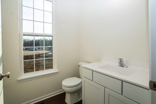 half bath with toilet, plenty of natural light, baseboards, and vanity