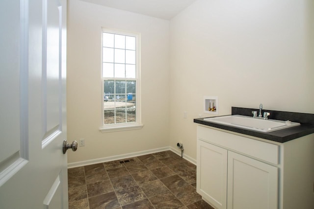 washroom with visible vents, baseboards, stone finish floor, hookup for a washing machine, and a sink