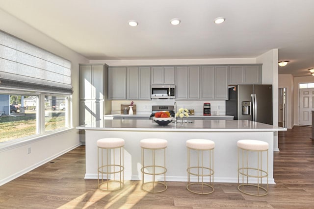 kitchen featuring an island with sink, appliances with stainless steel finishes, gray cabinets, and light countertops