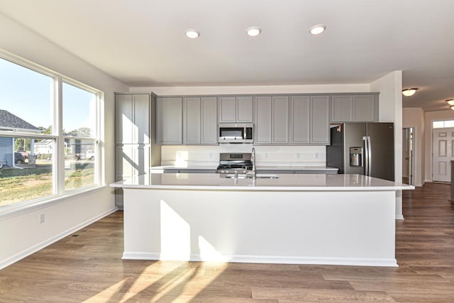 kitchen with a center island with sink, light countertops, gray cabinetry, appliances with stainless steel finishes, and a sink