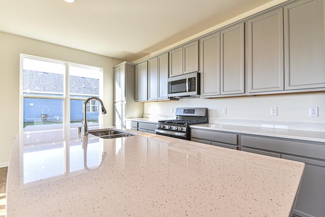 kitchen featuring stainless steel appliances, gray cabinets, a sink, and light stone counters