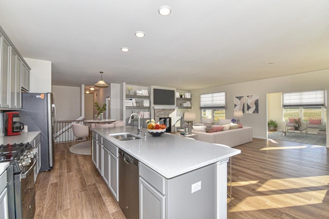 kitchen with stainless steel appliances, gray cabinetry, a sink, an island with sink, and wood finished floors