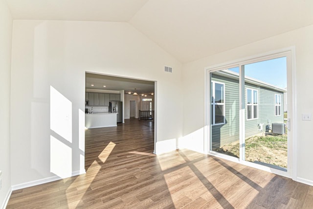 empty room with high vaulted ceiling, wood finished floors, visible vents, and baseboards